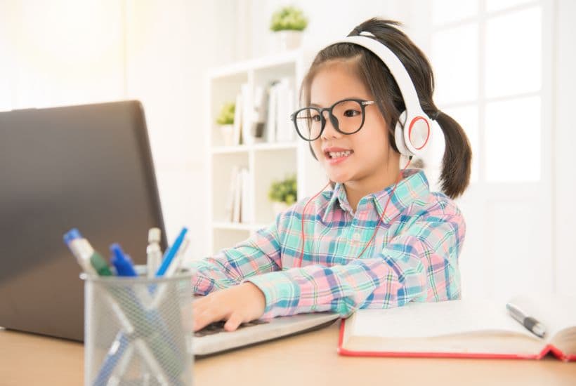 Young school girl wearing headphones and typing on a laptop.